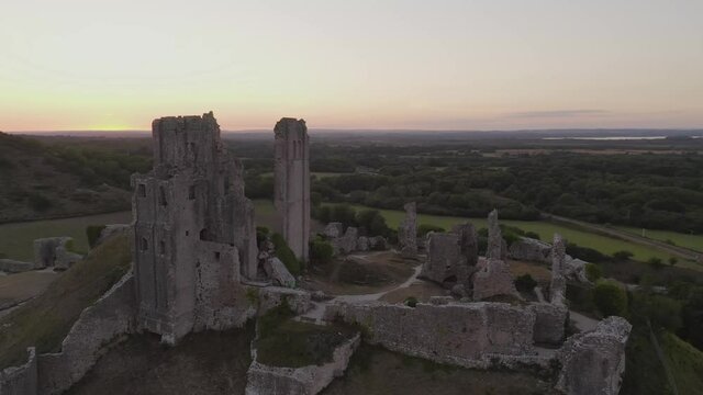 Aerial tracking around Corfe Castle ruins in Dorset, England at sunset
