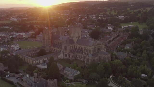 Wells, Somerset / United Kingdom (UK) - June 2020: Tracking aerial shot of Wells Cathedral with the sun setting in the background