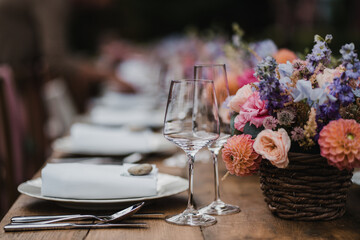 Wedding banquet wooden table decoration with wine glasses and plates with roses and flower bouquets catering decoration