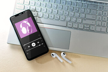 Smart phone with music app and laptop on desk, top view