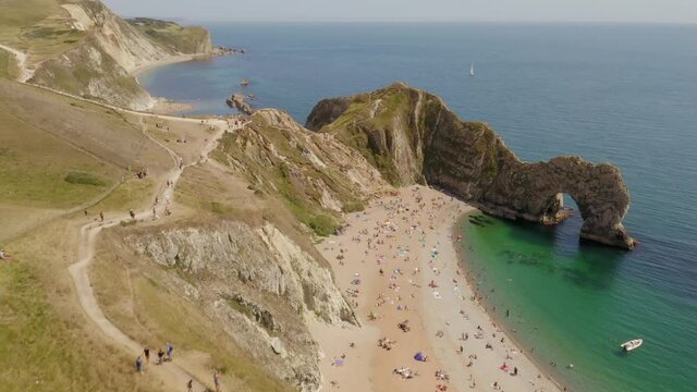 Rising aerial revealing tourists walking down to enjoy the famous beach by Durdle Door on Dorset's Jurassic Coast 