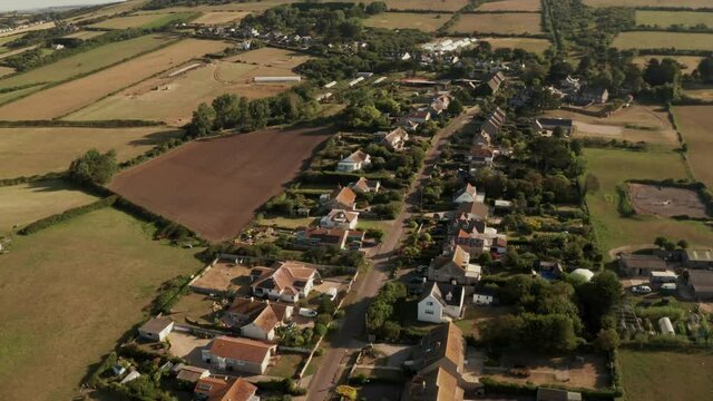 Tilting down aerial view of prosperous countryside village houses and gardens surrounded by green fields in Dorset, England