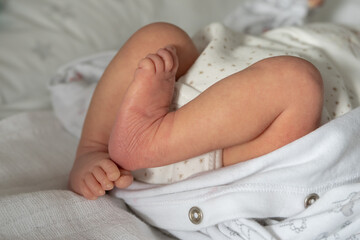 Close up on legs of newborn baby lying on the bed at home - unknown caucasian infant waiting to get dressed or undressed -growing up concept