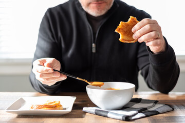 Middle age man eating a steaming bowl of tomato soup and a sandwich - 425157023