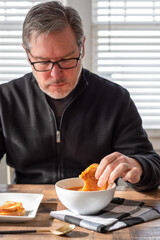 Middle age man dipping a grilled cheese sandwich in a bowl of soup