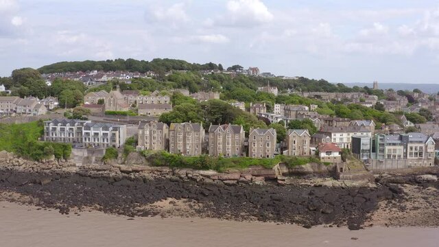 Aerial pullback from grand Victorian beach-front houses to reveal Clevedon Pier over the Severn Estuary on a sunny day