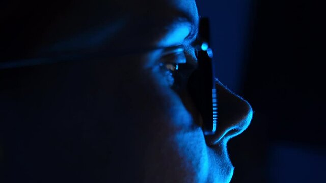Selective focus of young woman working on laptop. Close up side view of freelance girl in eyeglasses with reflections using computer in neon blue light. Freelance business woman with notebook at night