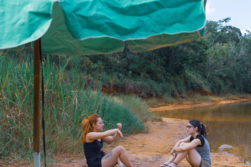 Two women talking sitting by the lake under a green parasol