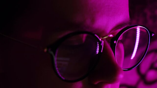 Selective focus of young woman look at computer pondering considering making notes, reflection of laptop screen with eyewear. Freelance girl with notebook at night. Distance online education concept