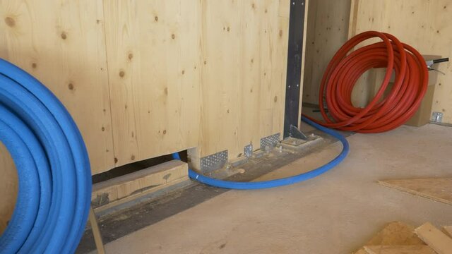 CLOSE UP: Coil of blue rubber tubing is rolled out underneath the wooden wall at a house under construction. Hot and cold water hoses are prepared for plumbing works at unfinished housing project.