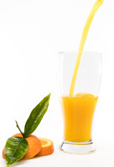 Pouring orange juice into glass with pieces of oranges and green leafs on black background.