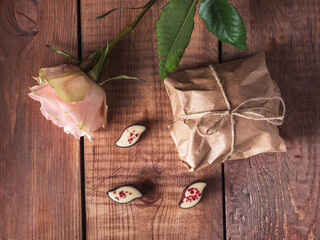 Greeting card with rose, sweets and gift in craft paper on wooden tray