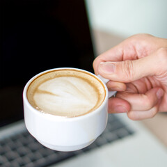 A cup of latte art coffee in hand.