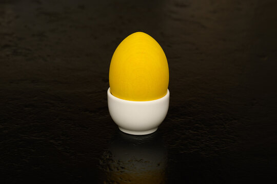 Yellow wooden egg in a white porcelain egg holder on a black background