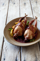 Oven baked quails served with berry sauce on stone plate close up