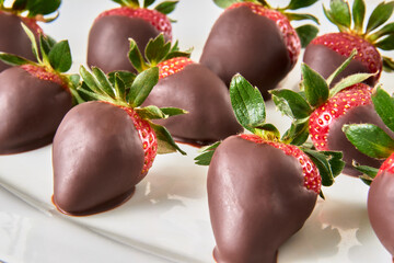 dark chocolate covered strawberries on a white plate on a marble table in close-up view. a gift for anniversaries, boyfriends or birthdays.