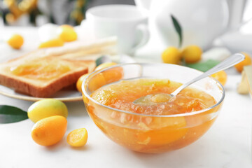 Delicious kumquat jam in glass bowl on white table, closeup