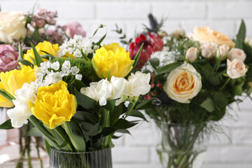 Beautiful bouquets with fresh flowers against white brick wall, closeup