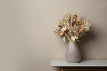 Beautiful dried flower bouquet in ceramic vase on white table near light grey wall. Space for text