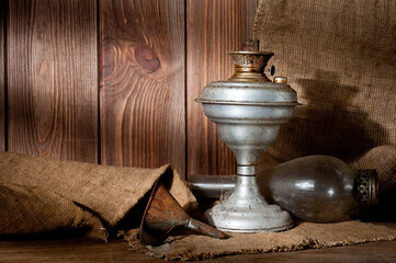 A vintage kerosene lamp covered in dust and soot, shot against a background of wood panels and burlap.