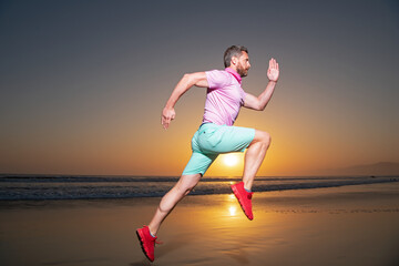 Fototapeta premium Athletic young man running in the nature. Fit man fitness model working outdoor by sea beach. Dynamic run movement.
