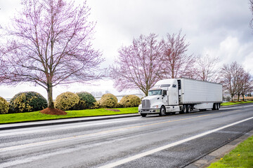 Bonnet big rig white big rig semi truck transporting cargo in refrigerator semi trailer running on...