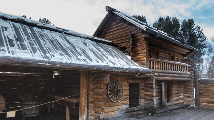 Naklejka premium An old wooden house with a balcony, built of logs and planks. Nearby there is an outbuilding. There is snow on the roof. Blue sky
