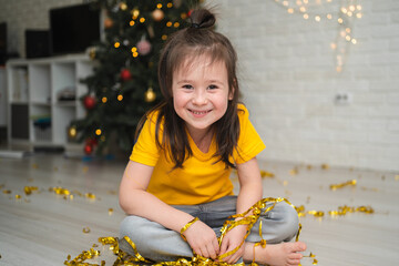 A joyful child catches tinsel. A bright children's holiday. A child in a yellow T-shirt catches a...