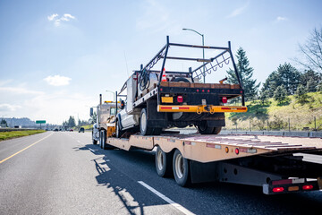 Powerful big rig semi truck transporting another truck on step down semi trailer driving on the...