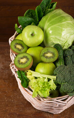 Green vegetables - kiwi, cabbage, herbs, celery, broccoli, cucumbers in a basket a wooden background