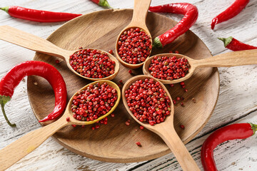 Spoons with red peppercorns on white wooden background