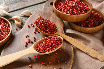 Bowls and spoons with red peppercorns on wooden background