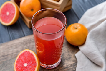Fresh grapefruits and glass of juice on color wooden background