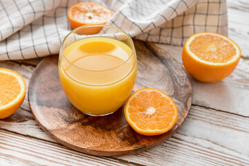 Fresh oranges and glass of juice on light wooden background