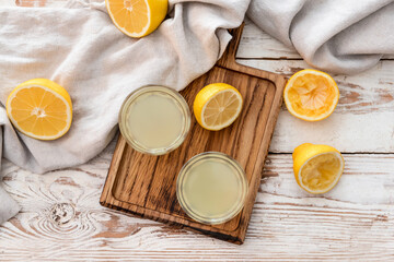 Fresh lemons and glasses of juice on light wooden background