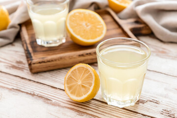 Fresh lemons and glasses of juice on light wooden background