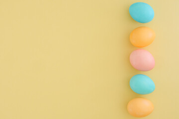 Minimalistic Easter composition of pastel colorful eggs in blue, yellow and pink colors on a pale yellow background. Copy space, top view, flat lay