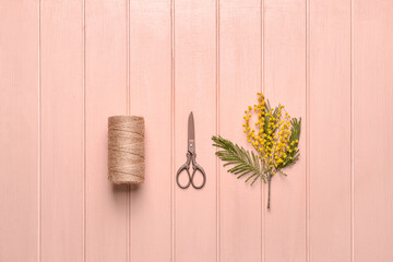 Beautiful blooming mimosa branch with scissors and threads on color wooden background