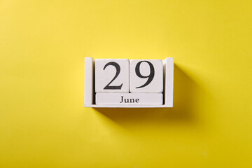 Wooden calendar on yellow background, top view, date 29 June