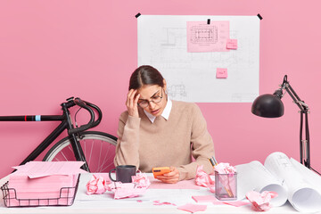 Overworked tired female architect focused at smartphone has much work to do works on architectural...