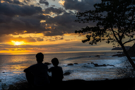 Beautiful picture of Father and son  watching the sunset in the pacific ocean in the magical beaches of Costa Rica