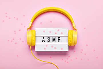 Yellow headphones, ASMR letters lightbox and confetti on pink background. ASMR Stress-relieving sounds concept, flat lay
