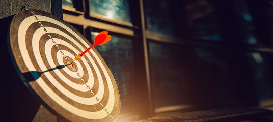 Dart arrow hit on bulleyes of dartboard to represent that the business reached the target  with dark tone picture style. Target and goal as concept. © kunakorn