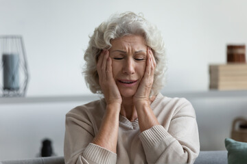 Fototapeta na wymiar Upset exhausted mature 60s woman suffering from headache or painful migraine at home. Stressed frustrated elderly lady feeling dizziness, holding head, touching temples with pain grimace. Head shot