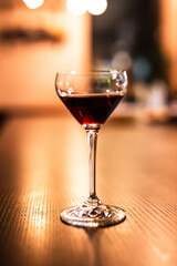 A coupe glass with red port wine at the bar counter. A vertical close up lifestyle photo with shallow depth of field.