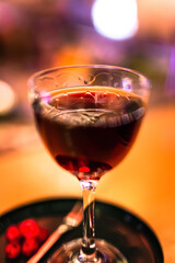 A red alcoholic cocktail in a nick and nora glass served on a tray with cranberry garnish. A lifestyle photo with shallow depth of field.