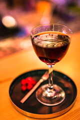 A red alcoholic cocktail in a nick and nora glass served on a tray with cranberry garnish. A lifestyle photo with shallow depth of field.