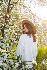 Smiling woman with the hat posing in blooming spring park. The concept of relax, travel, freedom and spring vacation. Fashion style.