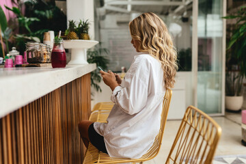 Stylish slim woman iin cafe while texting on smartphone and drinking cooling juice