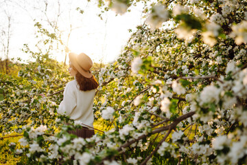 Smiling woman with the hat posing in blooming spring park. The concept of relax, travel, freedom and spring vacation. Fashion style.
